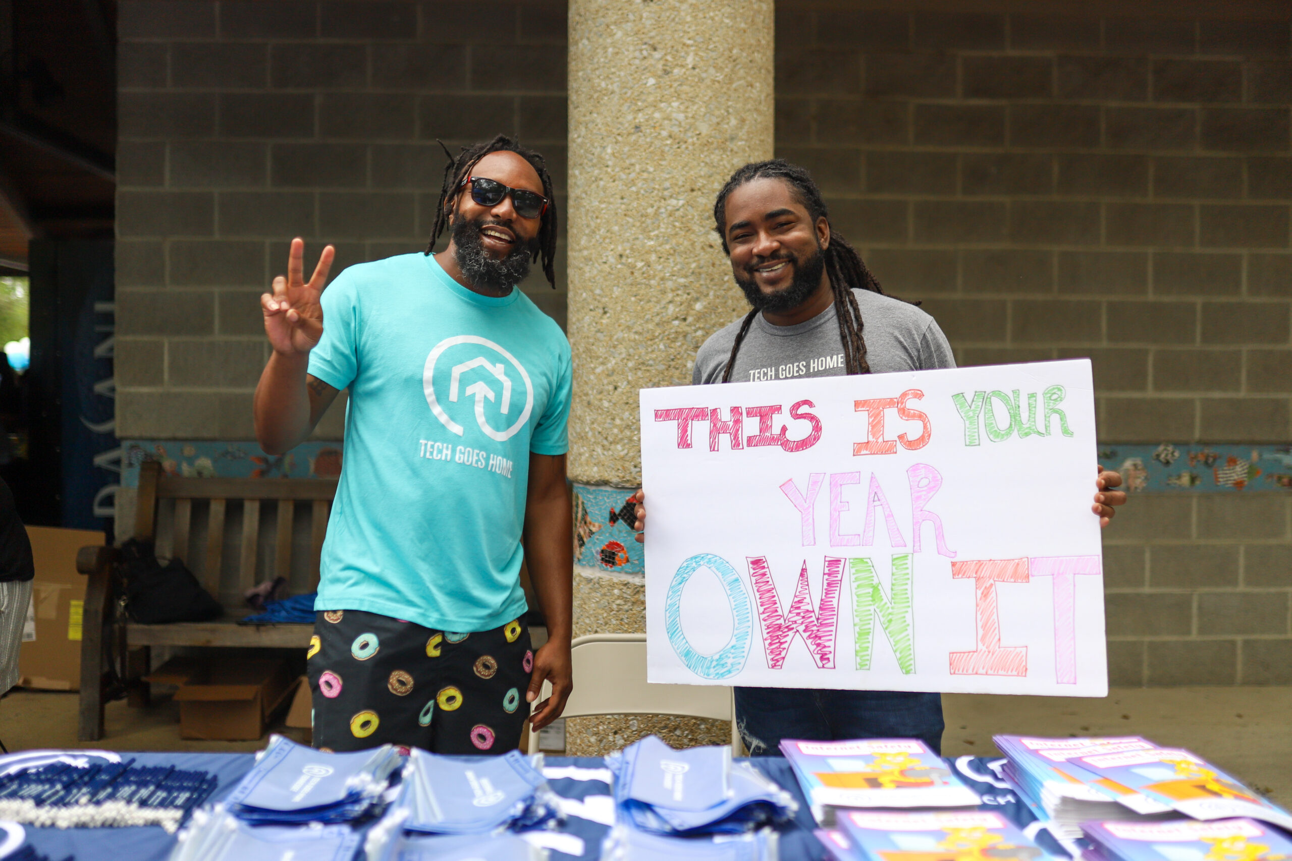 Two Tech Goes Home employees hold a sign saying, "This is my year—own it!" at the HCS Back 2 School Bash.