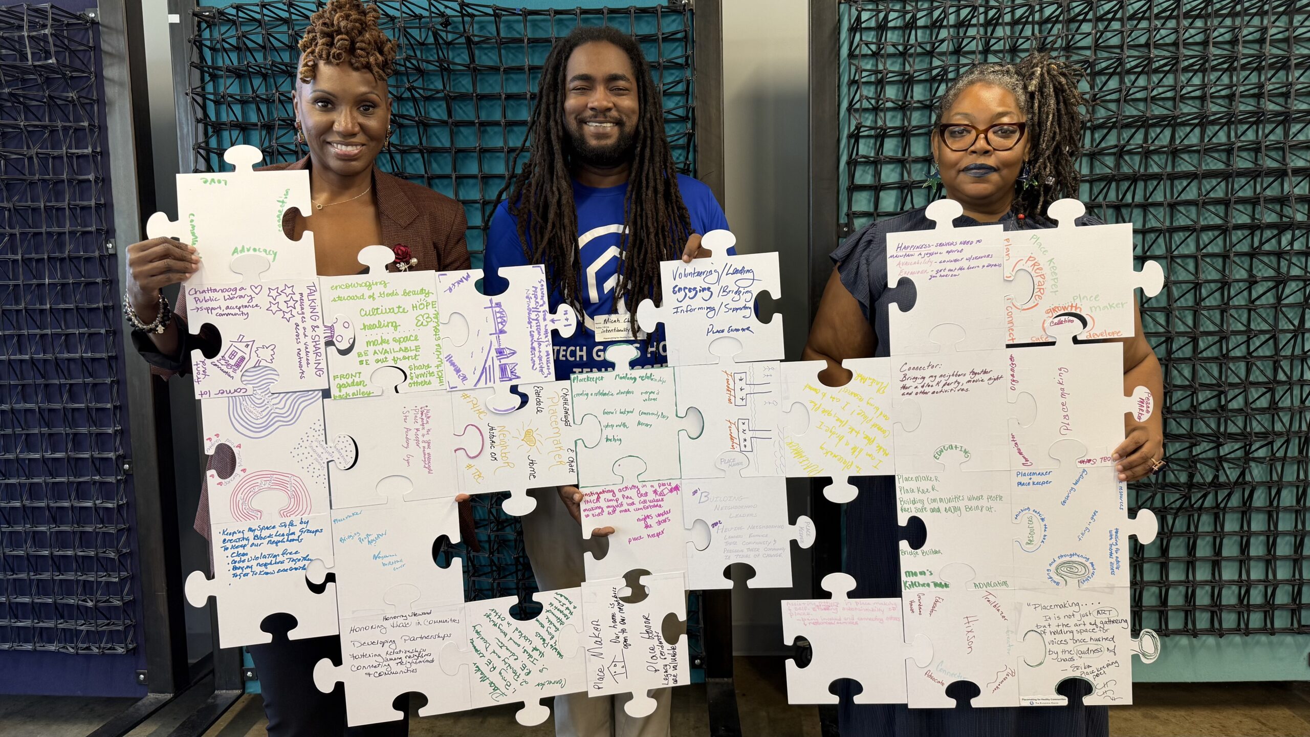 Three people are standing and holding a large puzzle with statements about placemaking written on each piece.