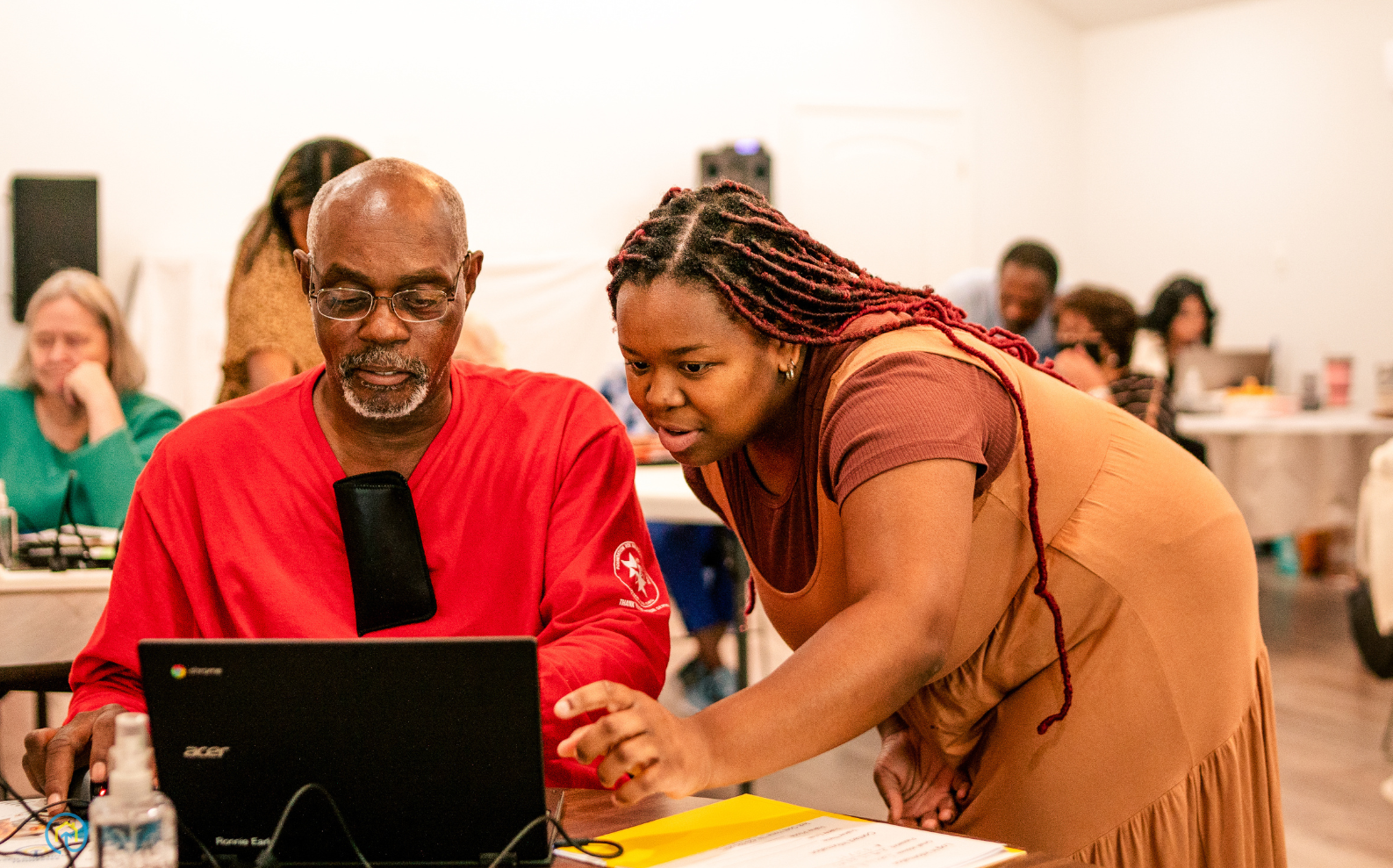 A woman points to something on a laptop to assist a man in a digital literacy class