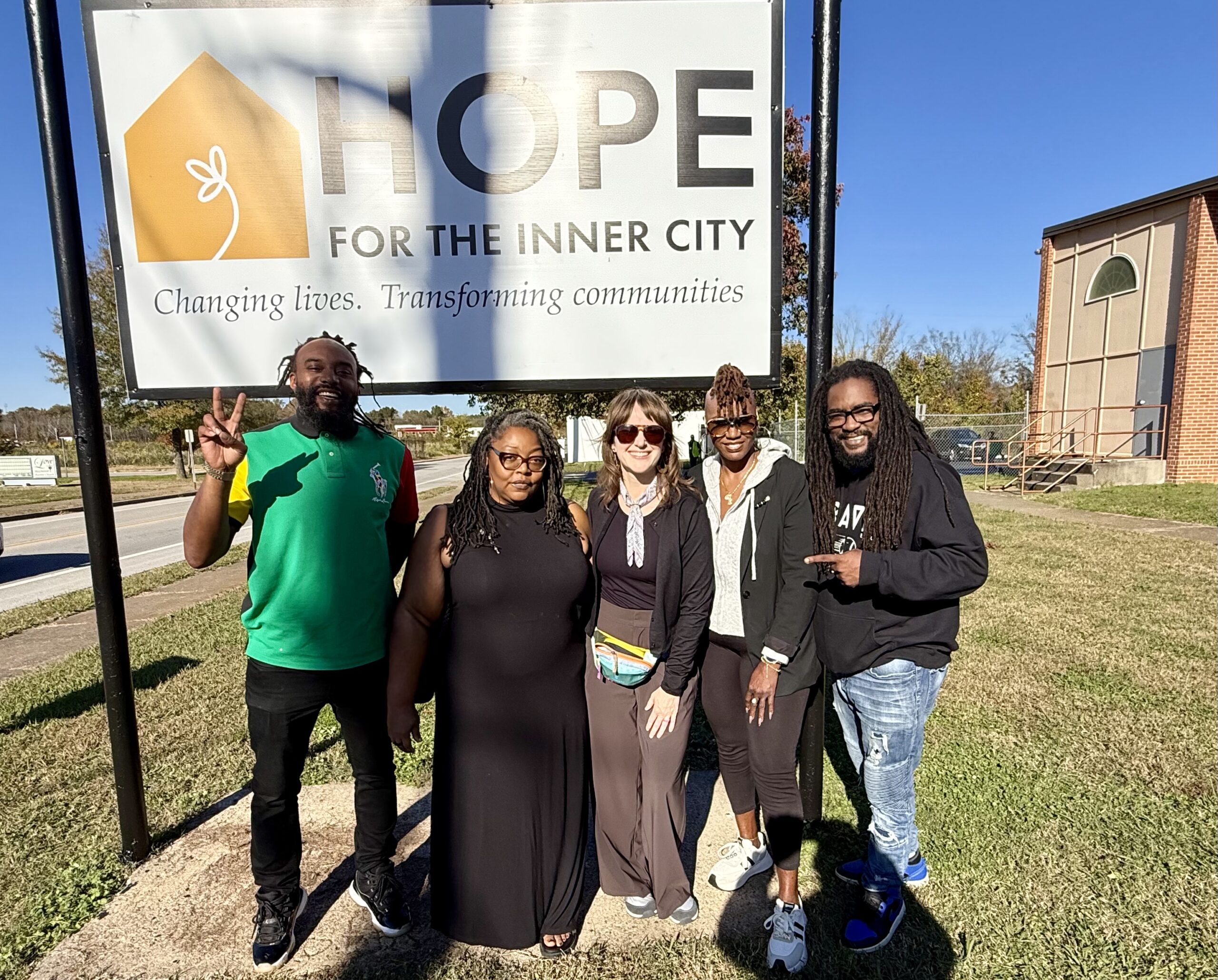 Two men and three women, smiling, stand in front of a sign that reads Hope for the Inner City.